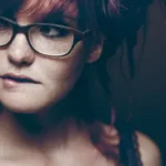 Woman with glasses and red hair, showcasing a thoughtful expression, reflecting the community and individual connection emphasized in Tap Tap rideshare experiences.