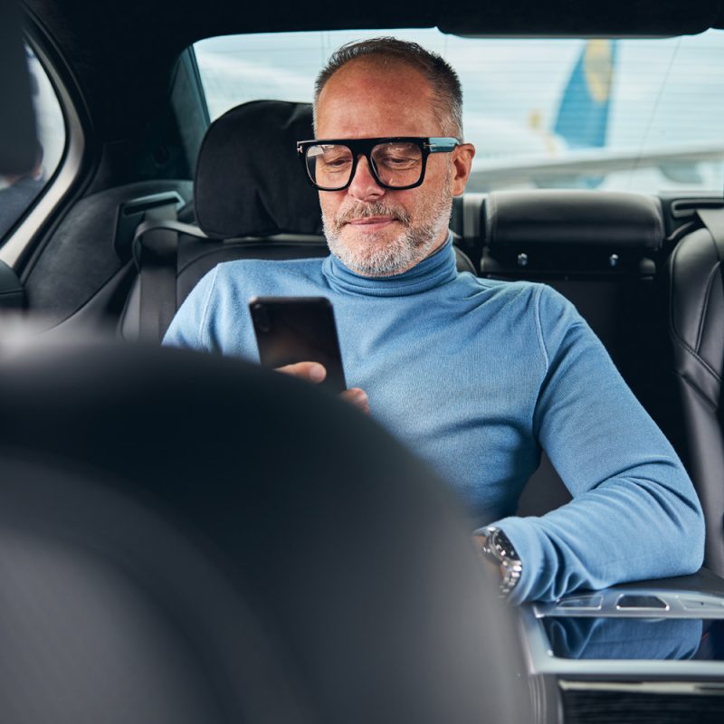 Man in a blue turtleneck sitting in the backseat of a car, using a smartphone, representing comfort and convenience in rideshare services.