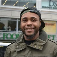 Smiling man wearing a cap and jacket, standing outside a grocery store, representing community engagement and customer satisfaction for TapTap rideshare service.