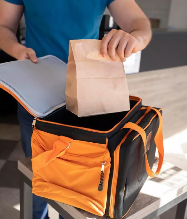 Person placing a paper bag into an orange and black insulated delivery bag, illustrating the grocery collection and delivery service offered by TapTap.