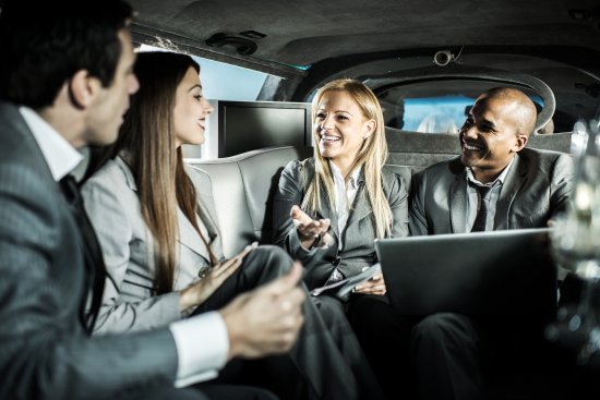 Group of professionals in business attire engaged in conversation inside a luxury limousine, highlighting a premium ride experience offered by TapTap rideshare services.